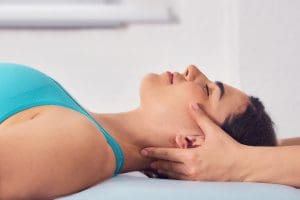 A smiling woman in a teal tank top has her head and spine adjusted